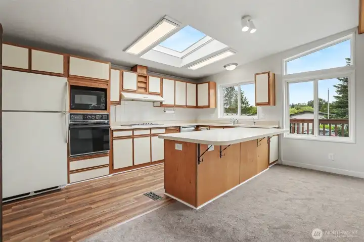 Spacious gourmet kitchen features new LVP flooring, skylights, wall oven, cooktop, western exposure and eating bar opening to the family room.