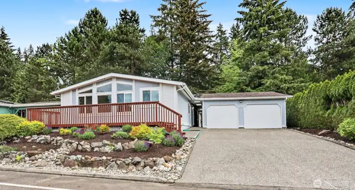 Street view with landscaped front yard and the large front wrap around deck and off street parking for 2 Plus cars plus a 2 car garage.