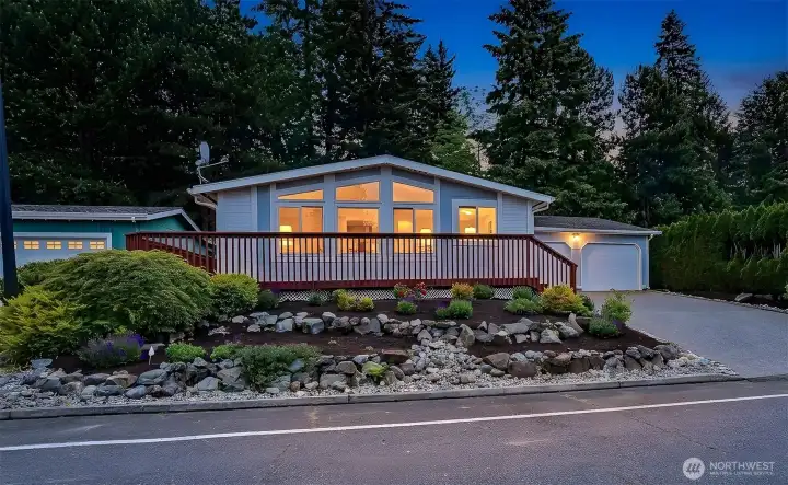 Street view with landscaped front yard and the large front wrap around deck.  Virtually staged twilight photo.
