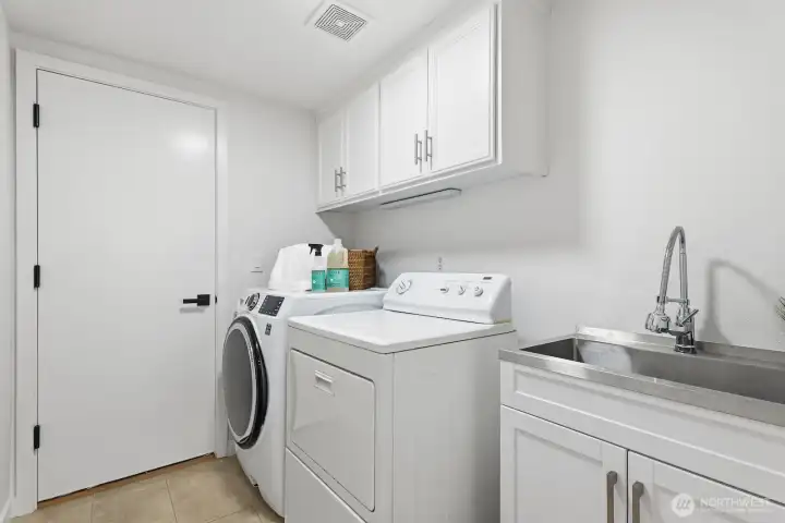 Main-floor utility/laundry room with utility sink, built-in cabinets, and tile flooring, conveniently located off the three car garage.
