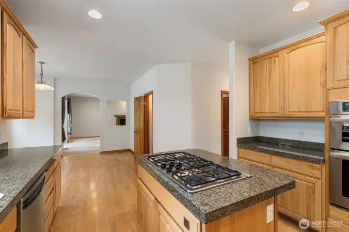 The 5-burner propane cooktop sits center stage on the granite island, with the great room visible beyond — the kitchen connects naturally to the rest of the main floor. The 5-burner propane cooktop sits center stage on the granite island, with the great room visible beyond — the kitchen connects naturally to the rest of the main floor.