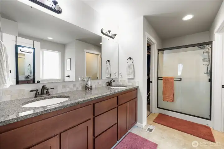 Tall double vanity with tile backsplash, large glass door shower with light above.