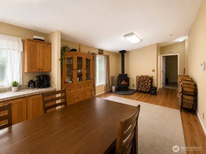 The dining area seamlessly connects to the living space, creating an inviting setting for everyday meals and gatherings. Warm wood cabinetry, durable flooring, and abundant natural light complement the home's comfortable design, while the nearby wood stove adds charm and a cozy atmosphere. The open layout provides excellent flow throughout the home, making entertaining and daily living both convenient and enjoyable.