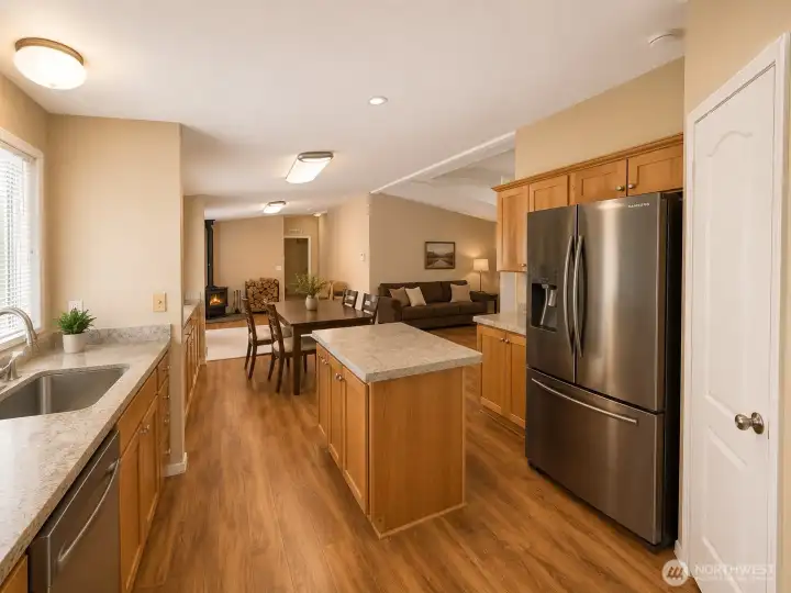 The spacious kitchen serves as the heart of the home, featuring abundant cabinetry, generous counter space, a center island for meal prep and gathering, and sleek stainless steel appliances. The open layout flows seamlessly into the dining and living areas, creating an ideal space for entertaining, family dinners, and everyday living. Warm wood finishes, durable flooring, and a cozy wood stove in the adjoining living area add comfort and character throughout this inviting central gathering space.