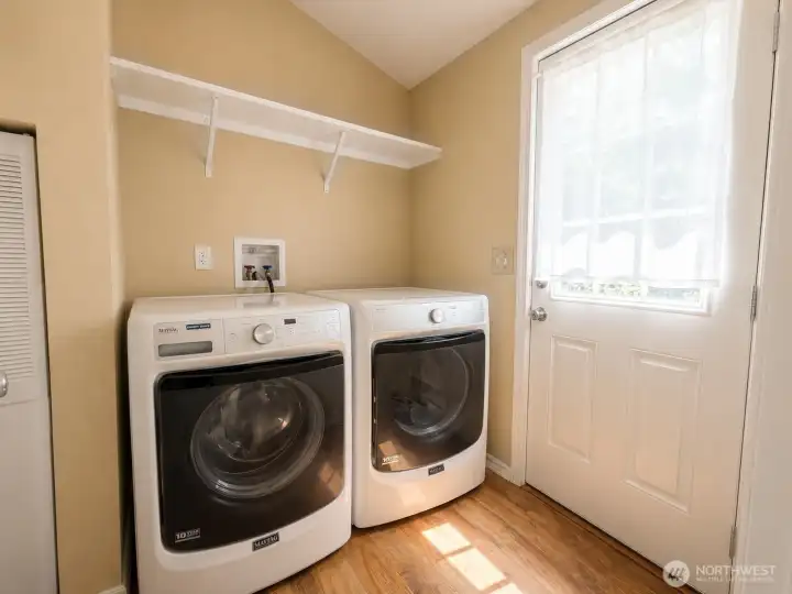 Convenient laundry room with modern front-load washer and dryer, durable flooring, and built-in shelving for added storage and organization. An exterior access door provides easy entry from outside, making this space ideal as a functional mudroom and laundry combination for everyday country living.