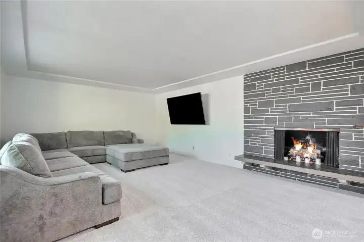 Large living room features a striking tray ceiling with lots of natural lighting, while a beautifully detailed fireplace anchors the space as its warm, inviting focal point.