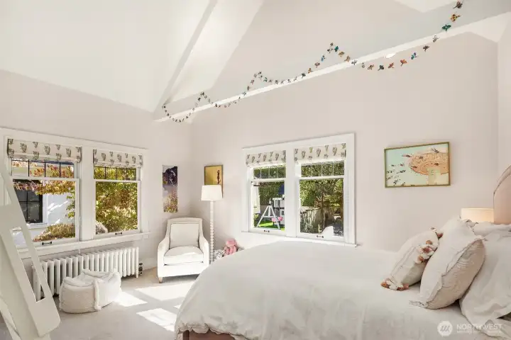 Enjoy vaulted ceilings and sun-drenched interiors in this bedroom, accented by elegant Roman shades.