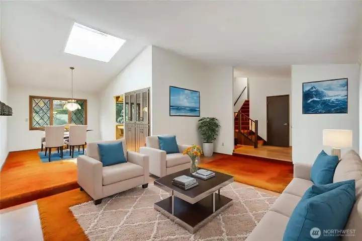 Virtually staged view of living room, dining room, partial view of kitchen, entry and staircase to 2nd floor