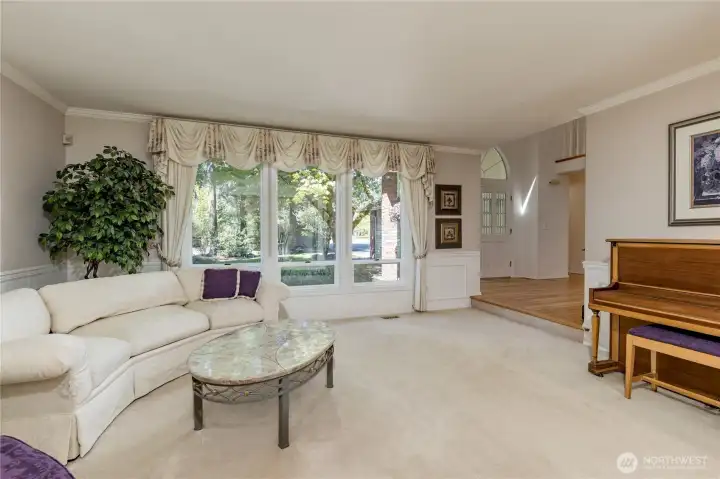Stately formal living room with timeless wainscoting, crown molding, and oversized windows that frame peaceful views of the private front yard