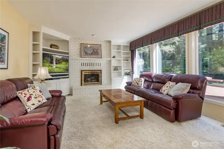 This sun-filled family room boasts extensive built-ins, a classic white brick fireplace, and massive windows that bring the beauty of the outdoors in.