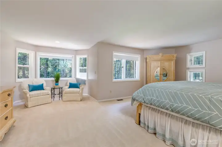 Your own private sanctuary! The expansive primary suite boasts a spacious sitting area surrounded by walls of windows, offering a peaceful spot to enjoy coffee while overlooking the park-like grounds.