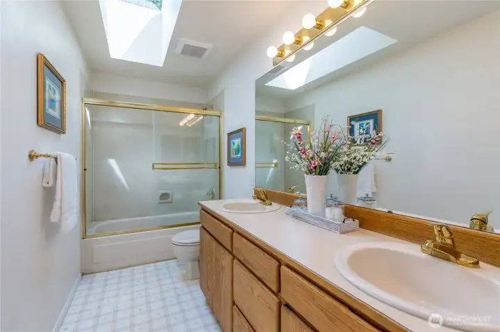 The upstairs full hallway bath is flooded with natural light from a large overhead skylight and features a dual-sink vanity, making morning routines easy for everyone.