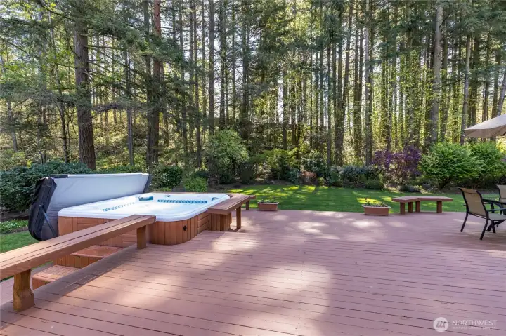 Expansive deck view highlighting the integrated hot tub and bench seating, all overlooking the lush, level lawn and majestic trees.