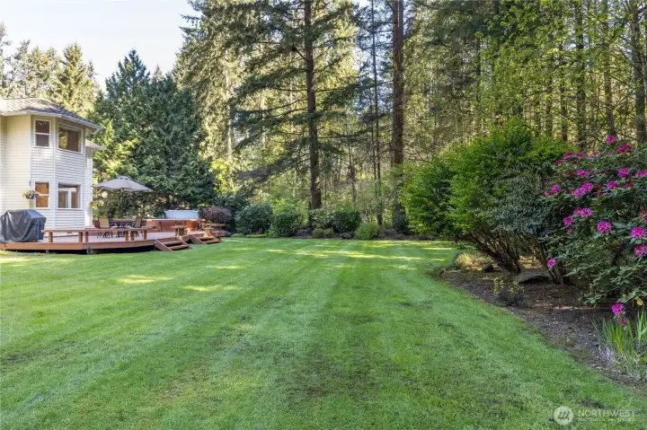 Beautifully landscaped garden beds with vibrant perennials border the expansive lawn, adding a splash of color to your private forest retreat.
