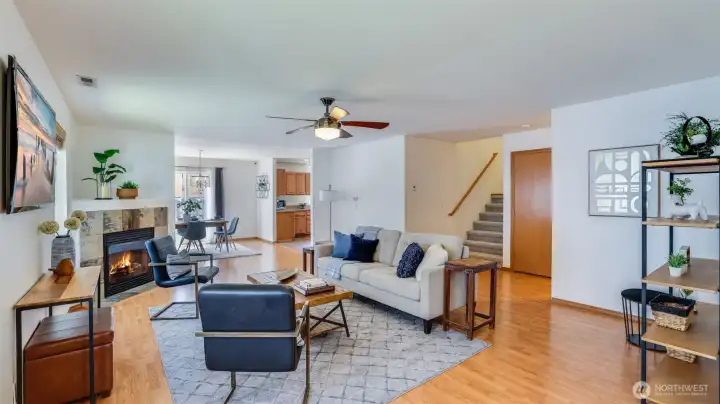 Enter into a living room with natural wood floors and a spacious, lofty layout that flows effortlessly into the kitchen, dining area, and staircase