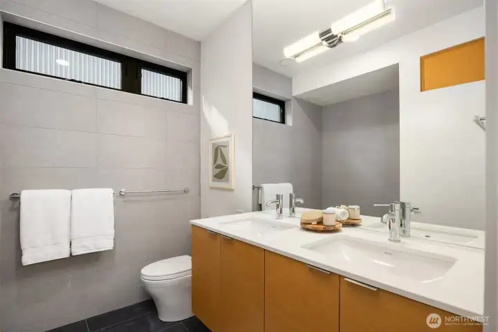 The bathroom maintains a consistent level of luxury including Abodian cabinetry, quartz countertops, ceramic tile floors, and Grohe WaterSense fixtures, reflecting a commitment to quality and sophistication that runs throughout the home.