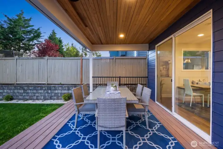 Entertain year round on the covered Trex deck featuring a wood slatted ceiling with integrated lighting and overhead heater, overlooking the professionally landscaped backyard with stone hardscape.