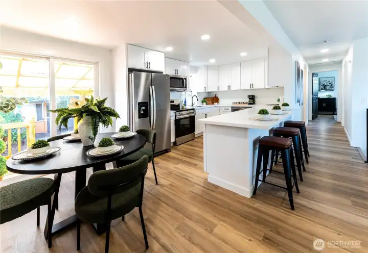 Kitchen and dining area with stainless appliances, white shaker cabinets, counter bar seating, and sliding doors to the covered deck. The whole space flows together beautifully.