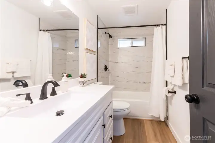 Remodeled full bath with double vanity, marble-style tile surround, and black fixture accents. Sharp.