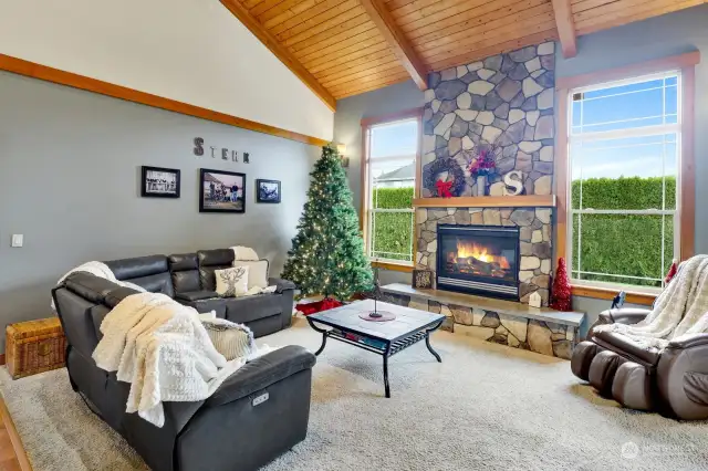 Enjoy this central, open-concept living area with a soaring vaulted ceiling, exposed wood beams, and a floor-to-ceiling stone fireplace as the focal point.