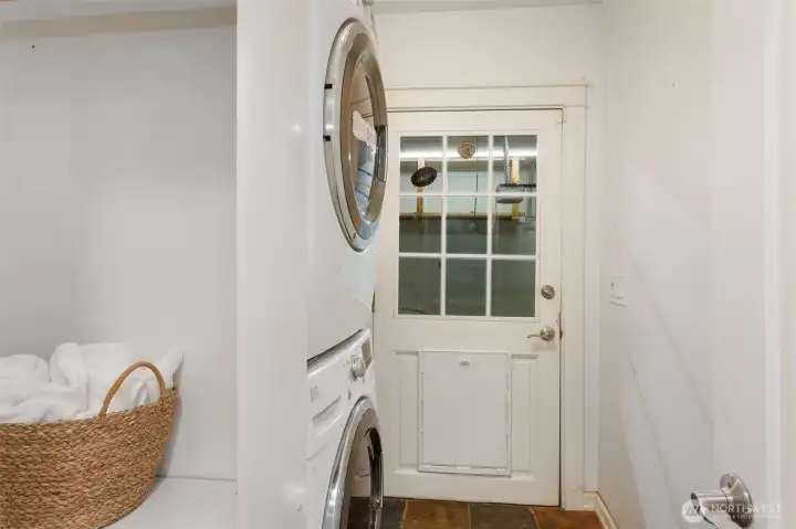 Laundry room leading out to garage.  Washer and dryer stay with home.  Sink to the right of appliances and storage shelving on other side