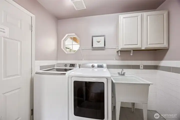 Sparkling clean laundry room is complete with utility tub and storage cabinet.