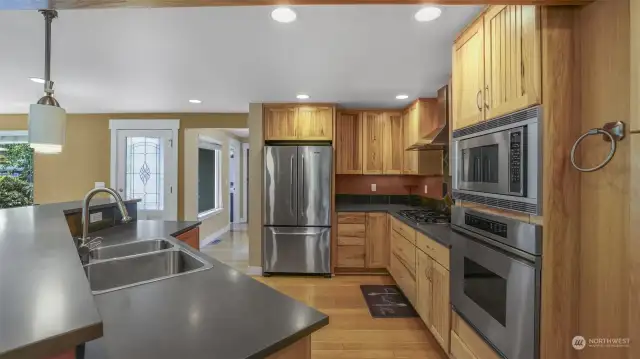 Kitchen boasts stainless steel appliances, Knotty Alder cabinetry, slate backsplash, large island with sink and bar top seating.