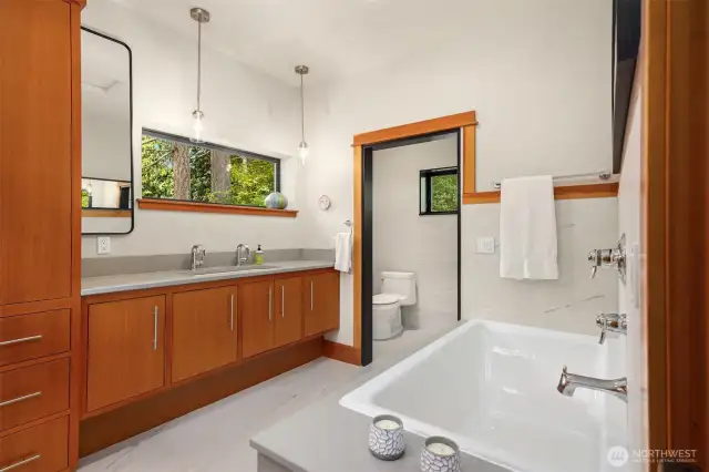 The primary bathroom with large tub and separate shower is filled with light.