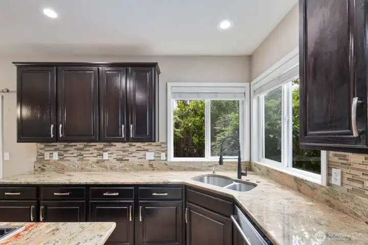 Large windows above the sink bring natural light into the kitchen while offering views of the surrounding greenery. Large windows above the sink bring natural light into the kitchen while offering views of the surrounding greenery.