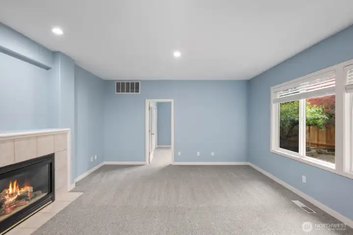 Spacious main-level room with a gas fireplace, recessed lighting, and large windows overlooking the backyard. Spacious main-level room with a gas fireplace, recessed lighting, and large windows overlooking the backyard.