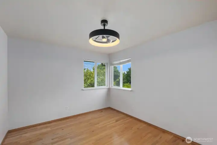 Light-filled bedroom featuring large corner windows and hardwood flooring. Multiple windows create a bright atmosphere while offering views of the surrounding neighborhood and greenery. Light-filled bedroom featuring large corner windows and hardwood flooring. Multiple windows create a bright atmosphere while offering views of the surrounding neighborhood and greenery.