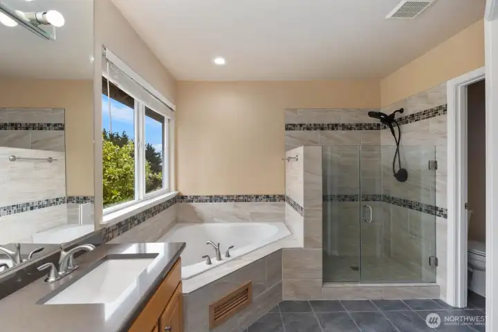 Primary bathroom featuring a corner soaking tub, glass-enclosed shower, large window, and spacious layout. Natural light and tile finishes create a bright and inviting space. Primary bathroom featuring a corner soaking tub, glass-enclosed shower, large window, and spacious layout. Natural light and tile finishes create a bright and inviting space.