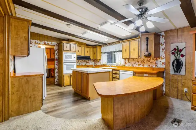 Nice large kitchen with an island, lots of cupboards, and a ceiling fan, adjacent to the living room.