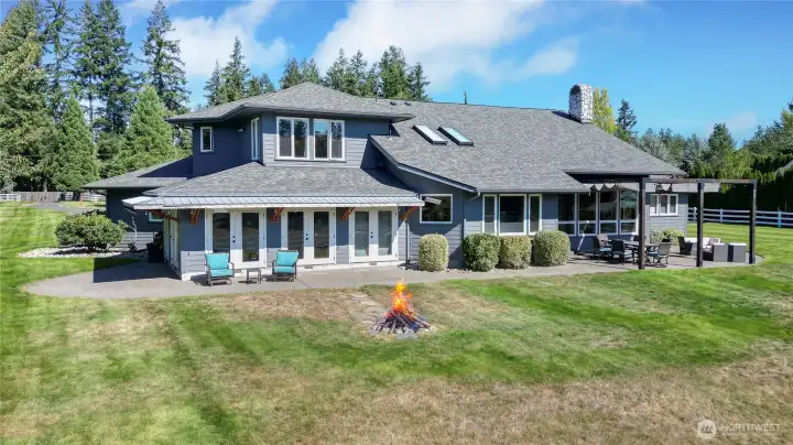 Drone view of the rear of the home. Upstairs is your expansive primary suite overlooking your back acres. I love the huge patio, the skylights and we have had so many amazing fires in that firepit. Just magical!