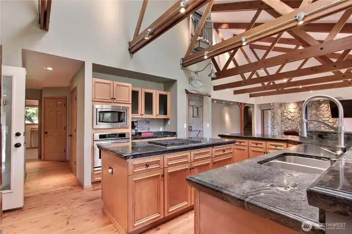 Kitchen view two, the beams and dramatic ceiling continues! To your left is the 4-season covered patio affectionately known as the White Room, down the hall to your left is the furnace room, water heater room and your utility room. We thought the chalkboard paint on those center cabinets was fun :)