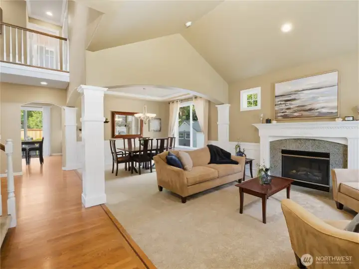 Light-filled living room featuring vaulted ceilings, oversized windows, custom millwork, and a stunning gas fireplace that creates a warm and inviting gathering space.