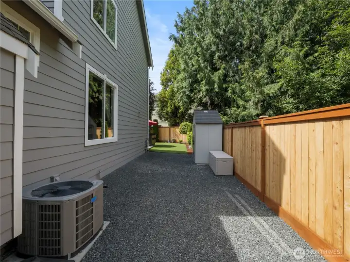 A fenced side yard with gravel pathway and storage shed provides convenient space for tools, seasonal items, and outdoor equipment.