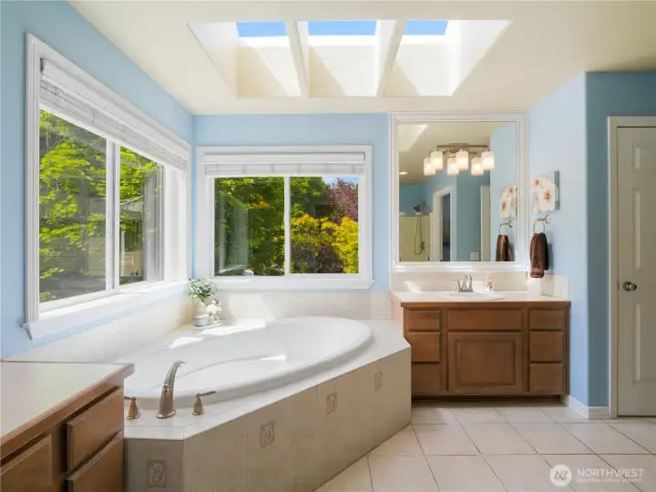 Primary bath offers a spa-inspired experience with a soaking tub, dual vanities, oversized windows, and tranquil views of the surrounding greenery.