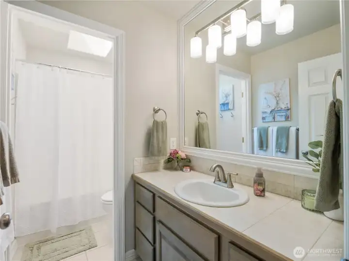 Secondary bathroom featuring a spacious vanity, ample counter space, updated lighting, and a skylight that fills the room with natural light.