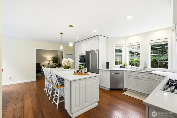 Updated chef’s kitchen with white cabinetry, stainless appliances, oversized island, and abundant windows capturing natural light and territorial views in this Lake Wilderness home.