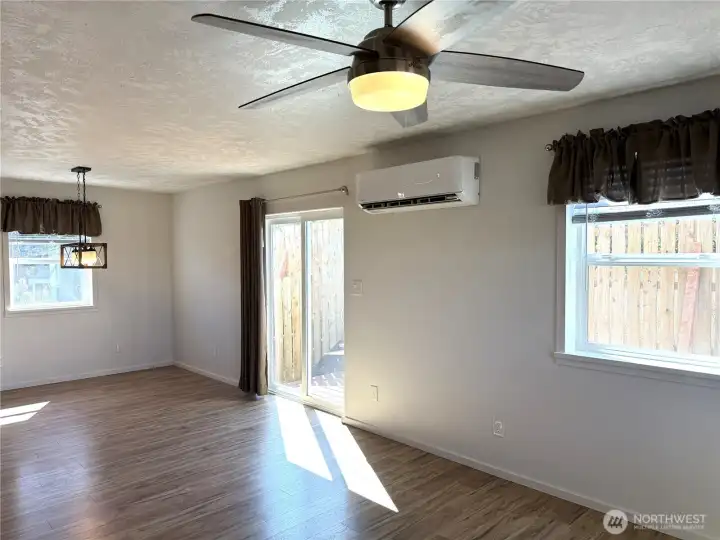 Showing the dining room with sliding doors on the south side. Note the ceiling fan and light in the foreground and the decorative lighting in the dining room. Ductless heating system.