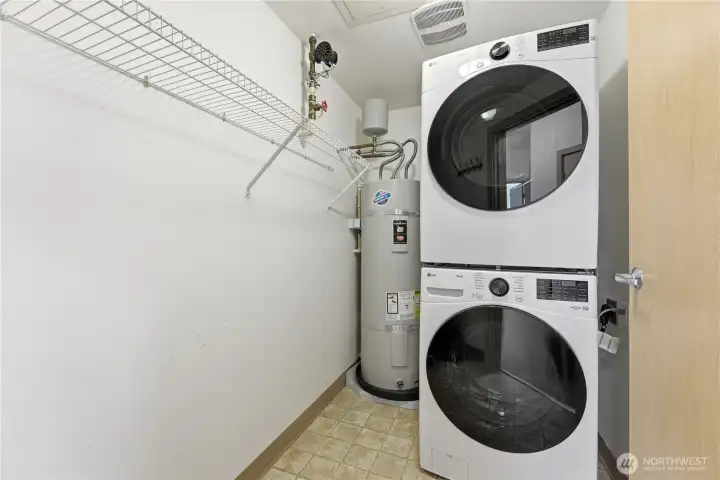 Large utility room with newer stackable laundry units, added storage, and a convenient coat rack