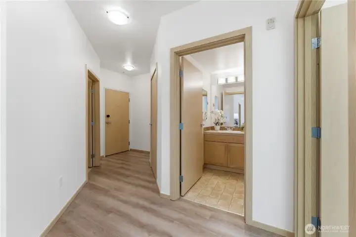 Entry hall with updated laminate floors, guest bathroom access, and the front door at the end of the corridor