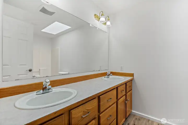 Full bath with 2 sinks, skylight, and new faux wood vinyl plank floors.
