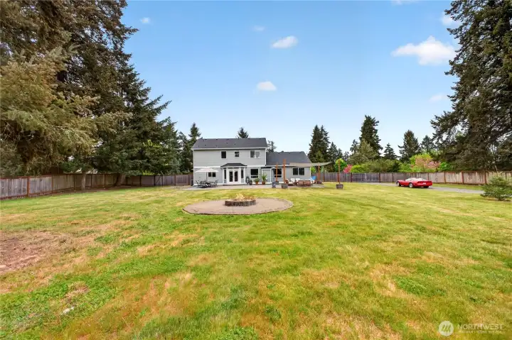 The backyard offers room for play, pets, gardening, and gatherings complete with a fire pit surrounded by gravel, mature landscaping, and plenty of space to enjoy the peaceful 1-acre setting.