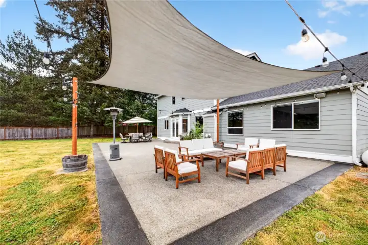 Enjoy the privacy and space of this beautifully maintained backyard featuring an expansive concrete patio that spans the length of the home—perfect for entertaining, outdoor dining, or relaxing evenings under the party lights.