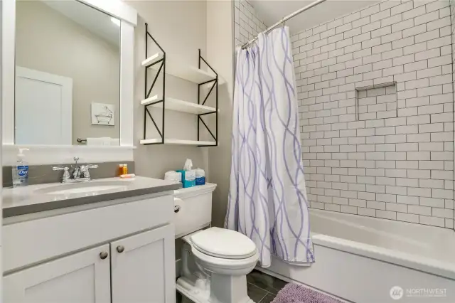 This upstairs bathroom has a large tub, full height tile surround, vanity with a quartz countertop, and a picture framed mirror- a classic upgrade!