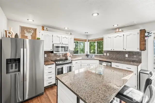 The bright kitchen has hardwood floors, stainless steel appliances, & granite counters