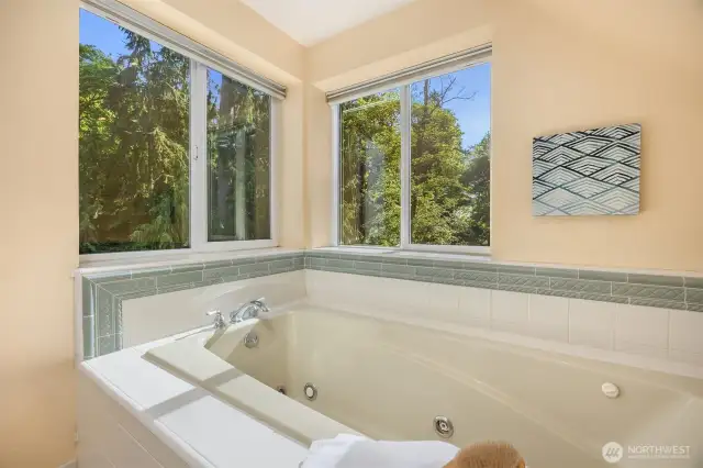 Serene soaking tub surrounded by two sets of windows that frame towering trees—offering both privacy and abundant natural light.