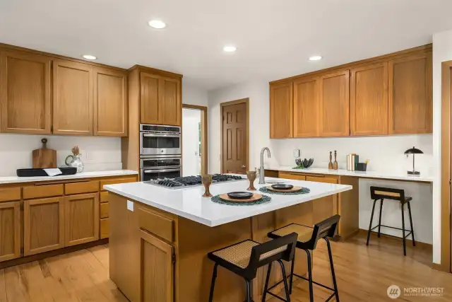 The spacious island offers casual seating, complemented by an adjacent built-in desk area - all with updated quartz countertops.  Just beyond, an oversized walk-in pantry sits near the pocket door leading to the nearby living room.